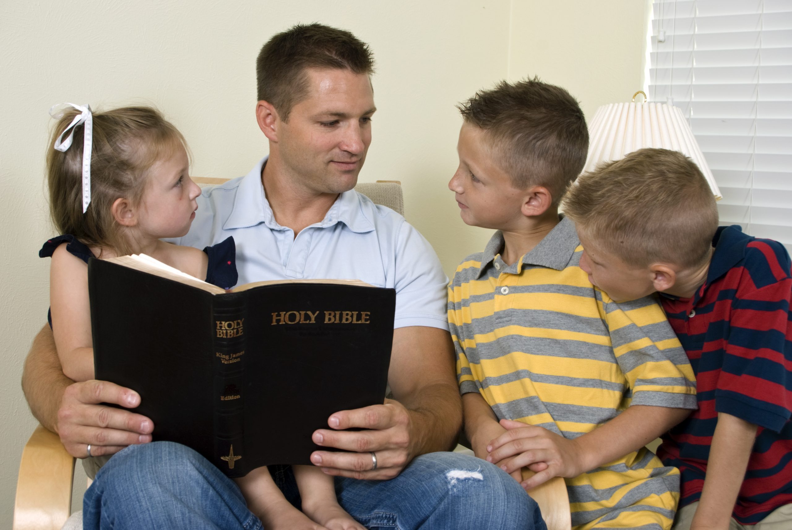 A father reads to his three young children from the Holy Bible.