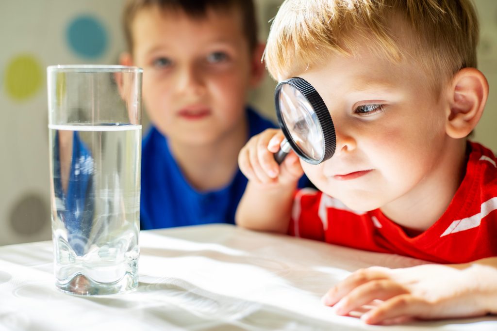 Child looking through magnifying glass with older child watching